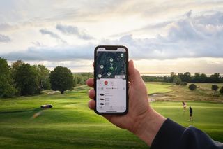 A person holding a smartphone with a fleet management app, overlooking a golfcourse.