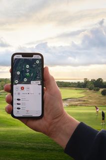 A person holding a smartphone with a fleet management app, overlooking a golfcourse.