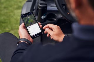Uma pessoa que utiliza uma aplicação para smartphone para monitorizar as atividades de tratamento da relva.
