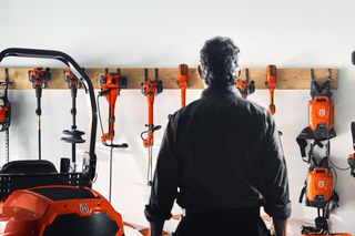 A person facing a wall rack displaying various Husqvarna gardening tools and equipment.