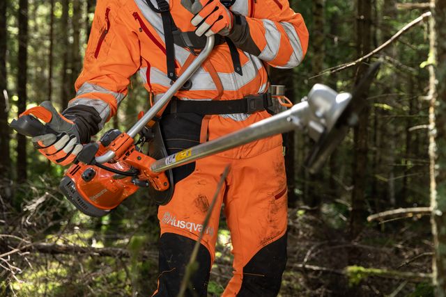 En person som använder en Husqvarna buskröjare i en skogsmiljö.