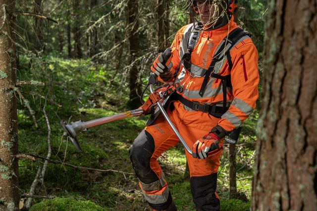 En person i arbetskläder som använder en buskröjare i en tät skog.