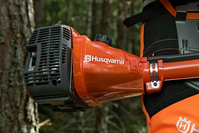 Närbild på en Husqvarna-produkt som bärs av en person i skogsmiljö.