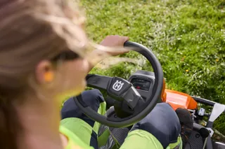 Een persoon die een zitmaaier bedient in een grasveld.