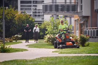 Een persoon die gazon maait met een zitmaaier in een woontuinomgeving.