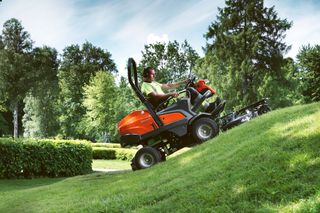 A person mowing lawn with a ride-on mower on a grassy slope in a garden.