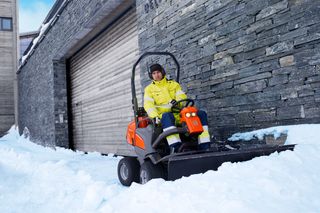 Een persoon die een sneeuwruimmachine bedient voor een stenen gebouw.