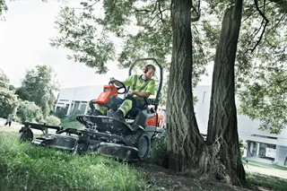 Une personne qui conduit une tondeuse autoportée près d’arbres dans une aire paysagée.