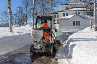 A person operating a snow removal machine on a snowy path near a house.