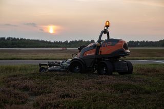 En professionell frontrotorklippare från Husqvarna som arbetar på ett gräsbevuxet fält i solnedgången.