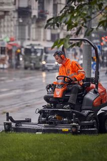 Inimene, kes kasutab niidukit linnatänava kõrval muruplatsil.