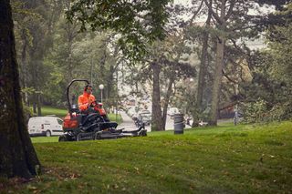 Eine Person, die einen Rider-Rasenmäher in einer Parkumgebung bedient.