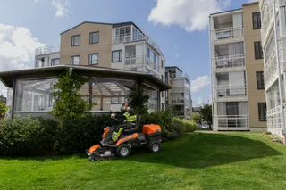 Iemand maait gras met een zitmaaier in een woontuin.