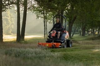 Osoba kosząca trawę kosiarką samojezdną w parku.