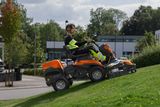 Iemand die gras maait met een zitmaaier op een grashelling in een tuin.