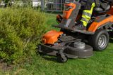 Iemand die gras maait met een zitmaaier in een tuin.