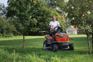 A person mowing lawn with a ride-on mower in a garden setting.