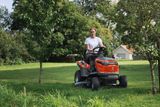A person mowing lawn with a ride-on mower in a garden setting.