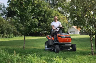 A person mowing lawn with a ride-on mower in a garden setting.