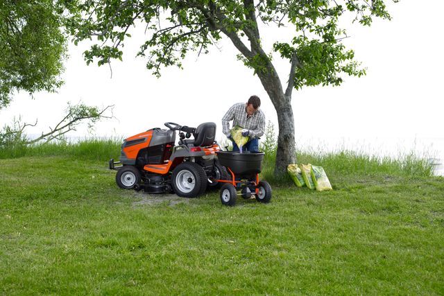 A person loading a ride-on mower with gardening supplies under a tree in a grassy area.