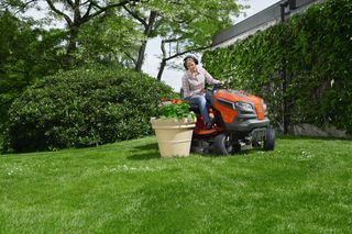 A person mowing a lawn with a ride-on mower in a garden setting.