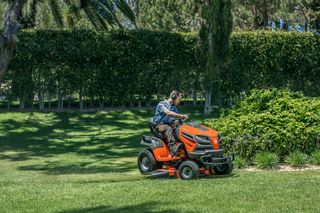 A person mowing lawn with a ride-on mower in a garden setting.