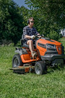 Osoba sekající trávník sekačkou s pojezdem na zahradě.