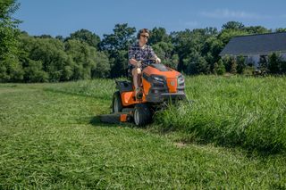 A person mowing a large lawn with a ride-on mower in a rural setting.