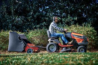 A person mowing lawn with a ride-on mower and a grass collector attached in a garden.