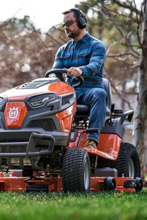 A person mowing lawn with a ride-on mower in a garden.