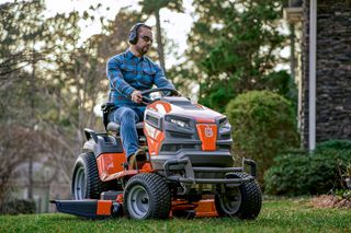 Eine Person, die mit einem Husqvarna Aufsitzmäher den Rasen in einem Garten mäht.