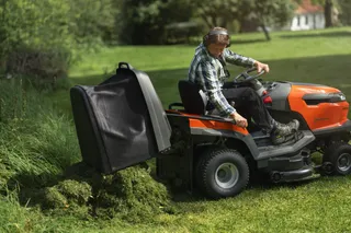 Een persoon die een zitmaaier bedient en gemaaid gras verzamelt in een tuin.