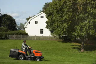Een persoon die een gazon maait met een zitmaaier in een tuinomgeving.