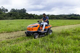 A person mowing lawn with a ride-on mower in a grassy field.