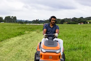 A person mowing lawn with a ride-on mower in a grassy field.
