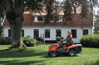 A person mowing a lawn with a ride-on mower in a garden setting.