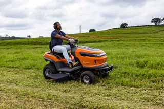 A person mowing lawn with a ride-on mower in a grassy field.