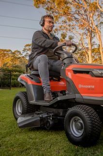 A person riding a Husqvarna ride-on mower in a garden setting.