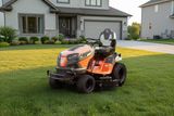A Husqvarna ride-on mower parked on a well-maintained lawn in front of a modern house.