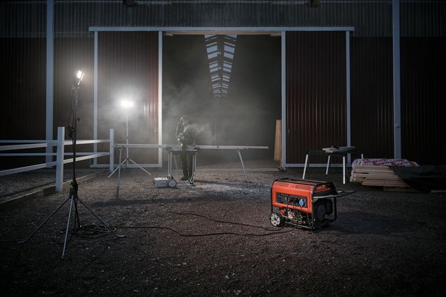 A person working at a table with a generator in a dimly lit barn setting.