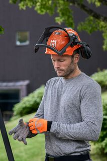 Una persona, che indossa attrezzatura da lavoro e guanti, che si prepara a utilizzare un potatore ad asta su un ramo di un albero.