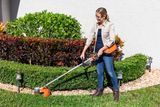 A person using a string trimmer to edge a garden lawn.