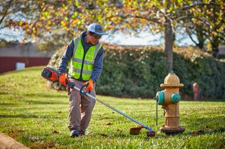 A person using a grass trimmer near a fire hydrant in a park setting.