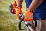 A person holding a Husqvarna product with both hands, wearing orange gloves.