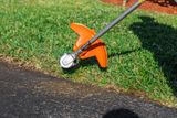 A grass trimmer being used to edge a lawn along a paved surface.