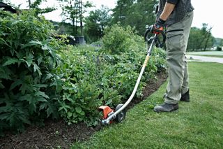 A person using a grass trimmer to edge a garden bed.