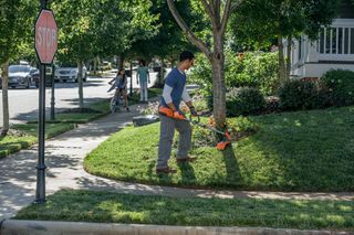 A person using a grass trimmer to edge a lawn in a suburban neighborhood.