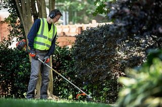 En person som använder en grästrimmer för att underhålla kanterna på en gräsmatta i trädgården.