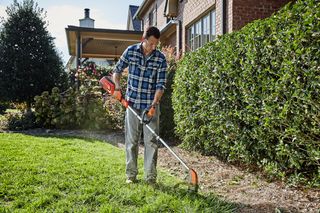 A person using a grass trimmer to edge a lawn in a residential garden.