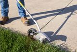 A person using a lawn edger to trim grass along a concrete pathway.